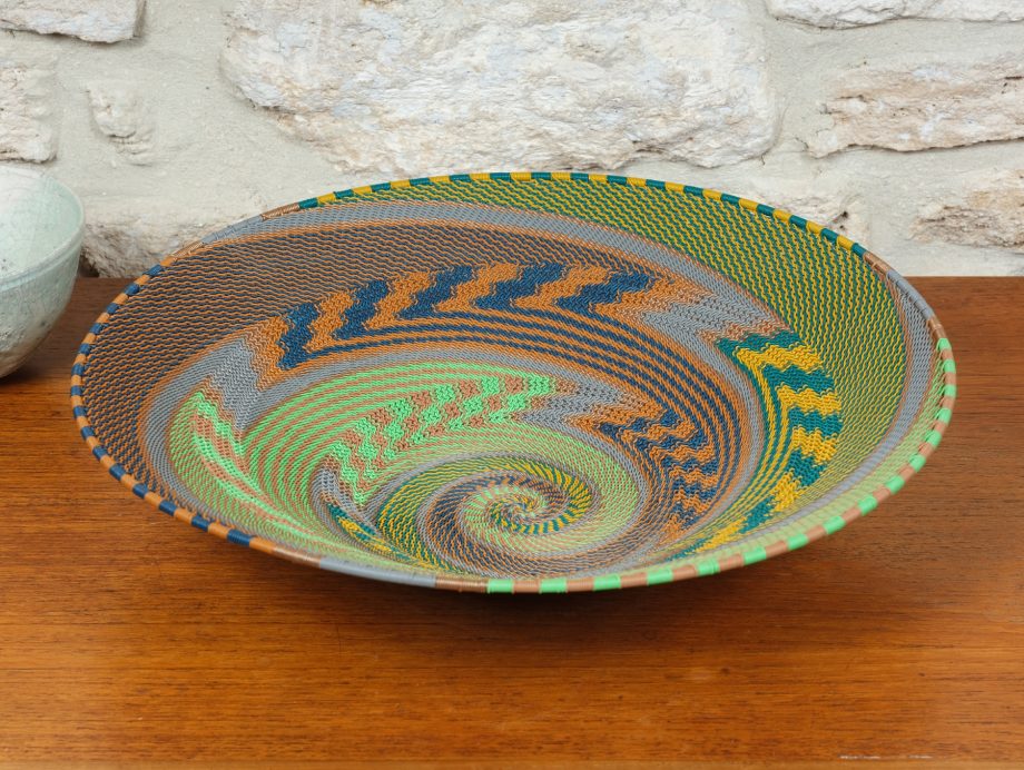 Assiette tressée en fil de téléphone Zoulou aux couleurs chatoyantes et au motif singulier, une pièce d'artisanat africain unique.